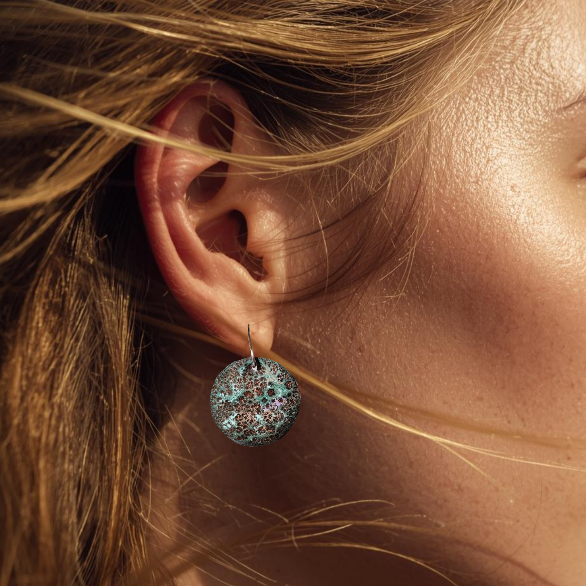 Close-up of an ear wearing a textured copper earring with blonde hair.