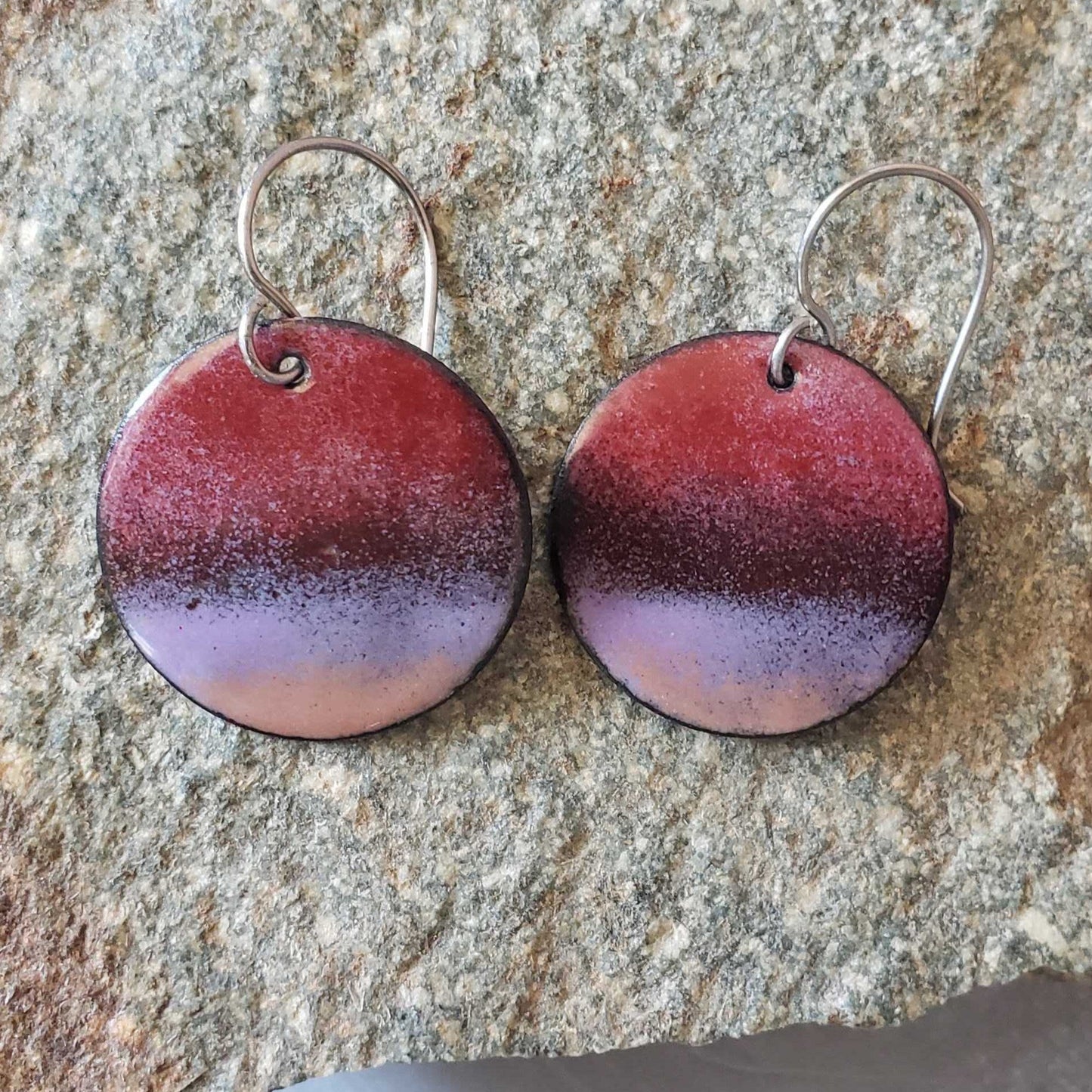 Pair of round copper earrings with a gradient design on a textured stone surface
