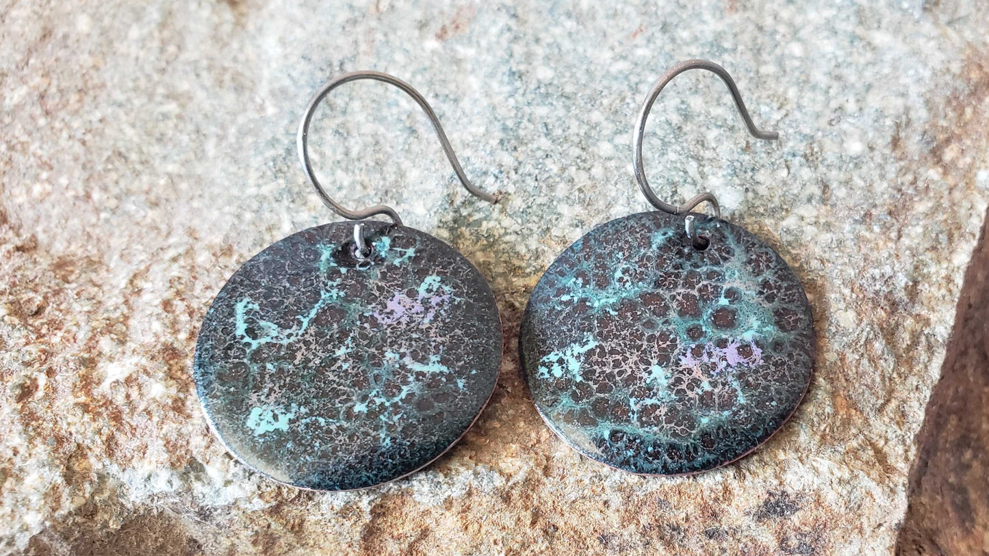 Pair of round copper earrings with a textured surface on a stone background
