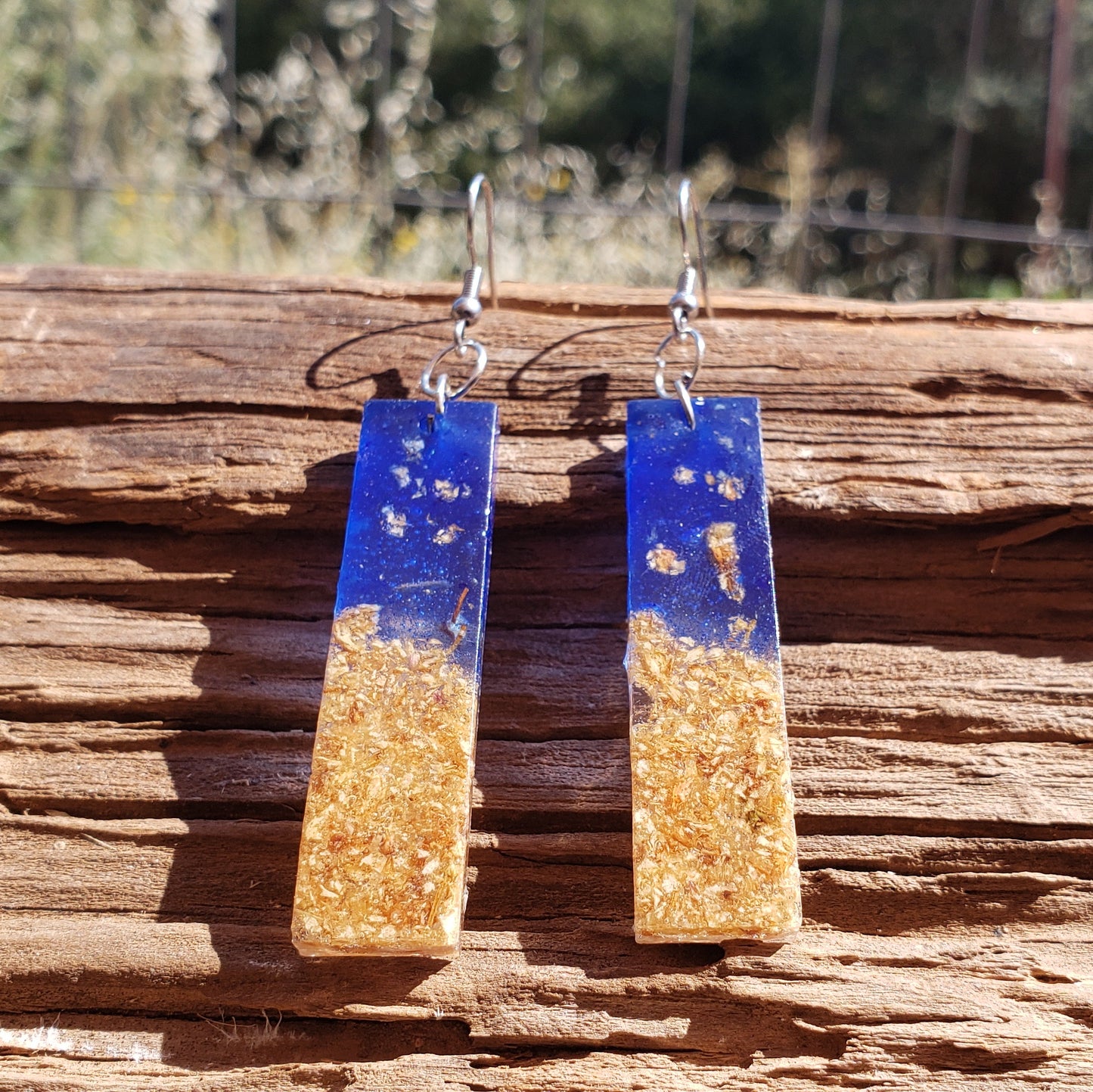 Pair of blue and gold earrings with dried flowers on a wooden surface