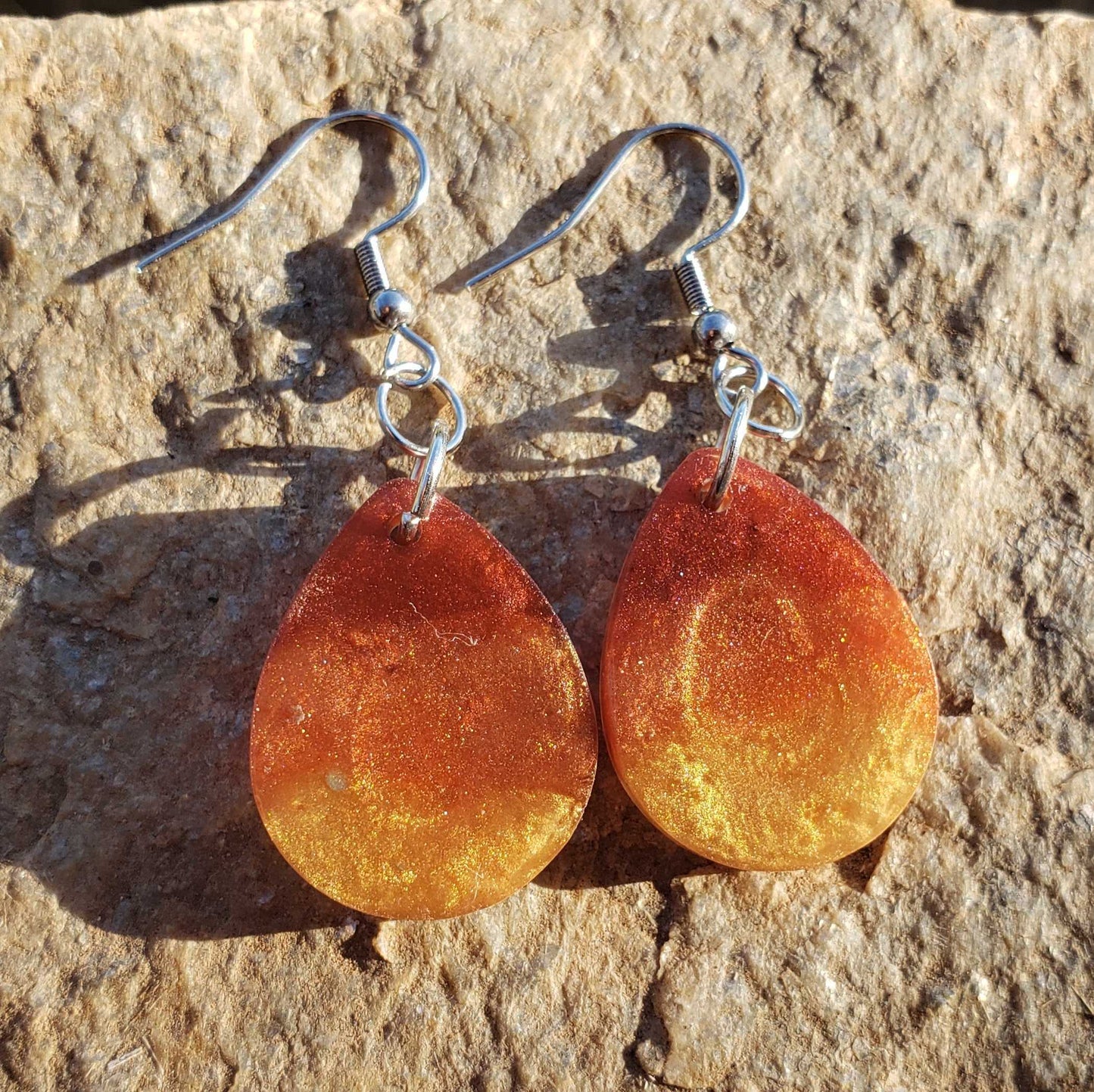 Pair of orange flame fire colored teardrop earrings on a stone background