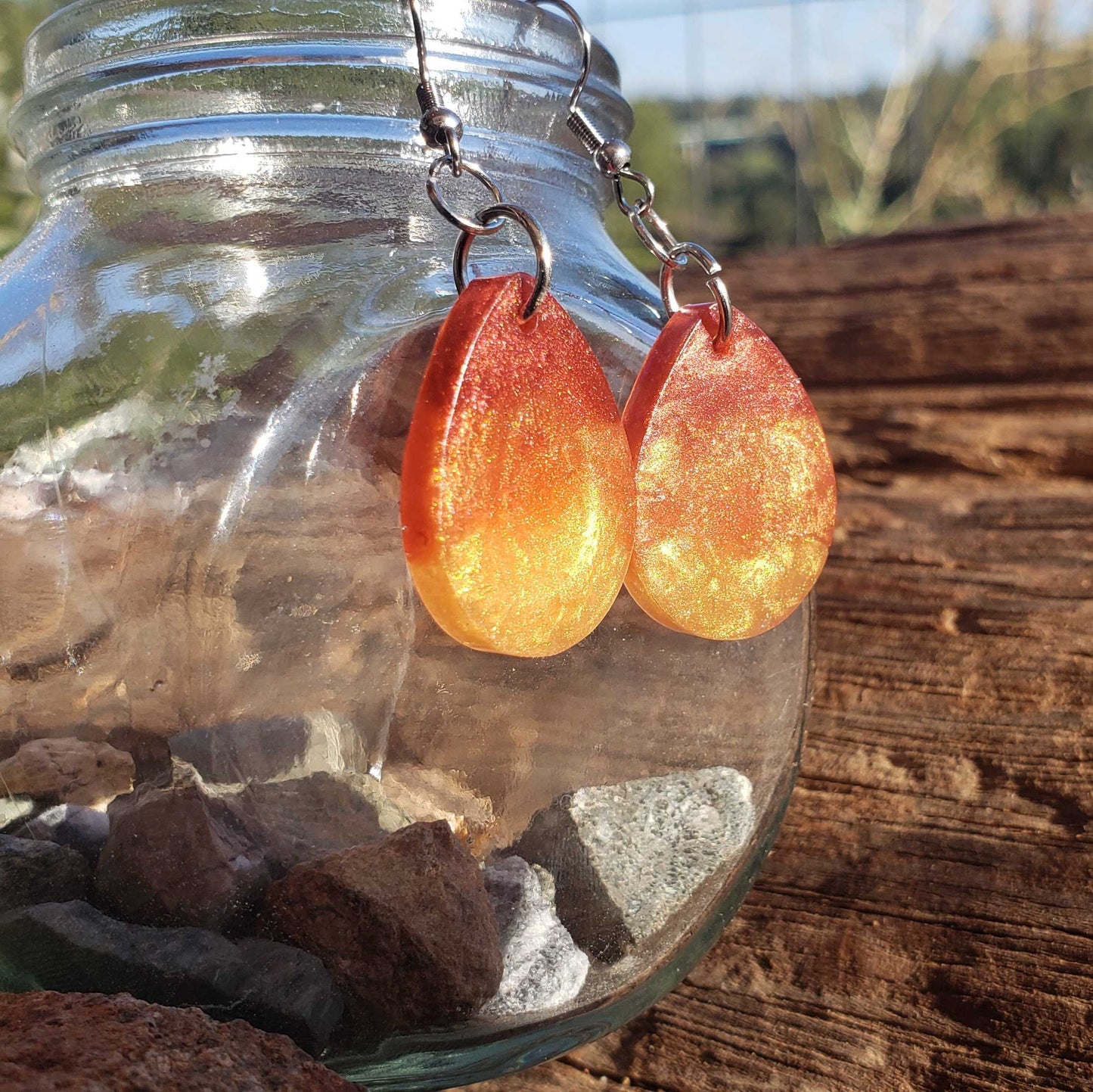 Orange flame fire colored teardrop earrings hanging from a glass jar on a wooden surface.