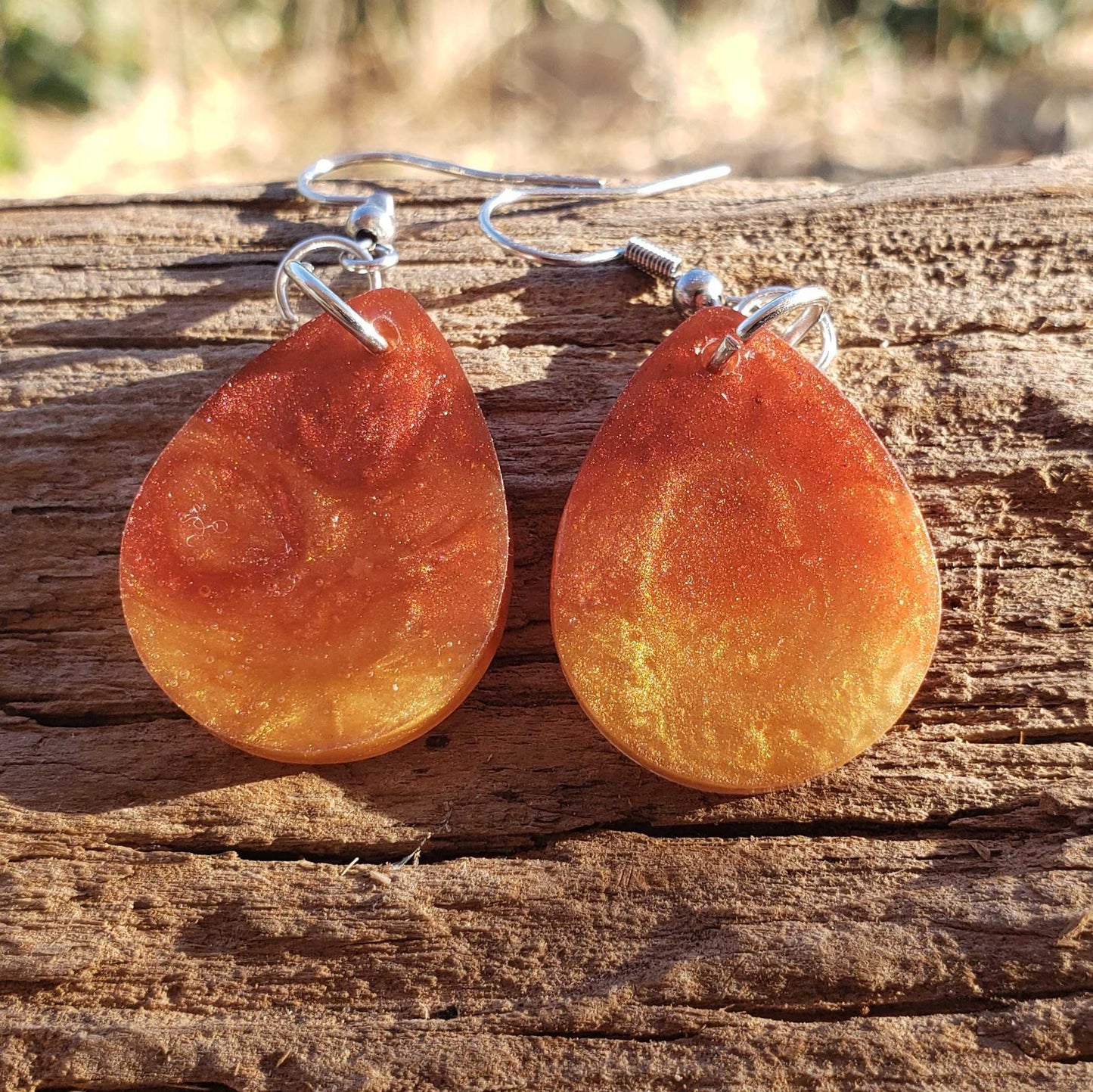 Teardrop-shaped fire flame orange earrings on a wooden surface