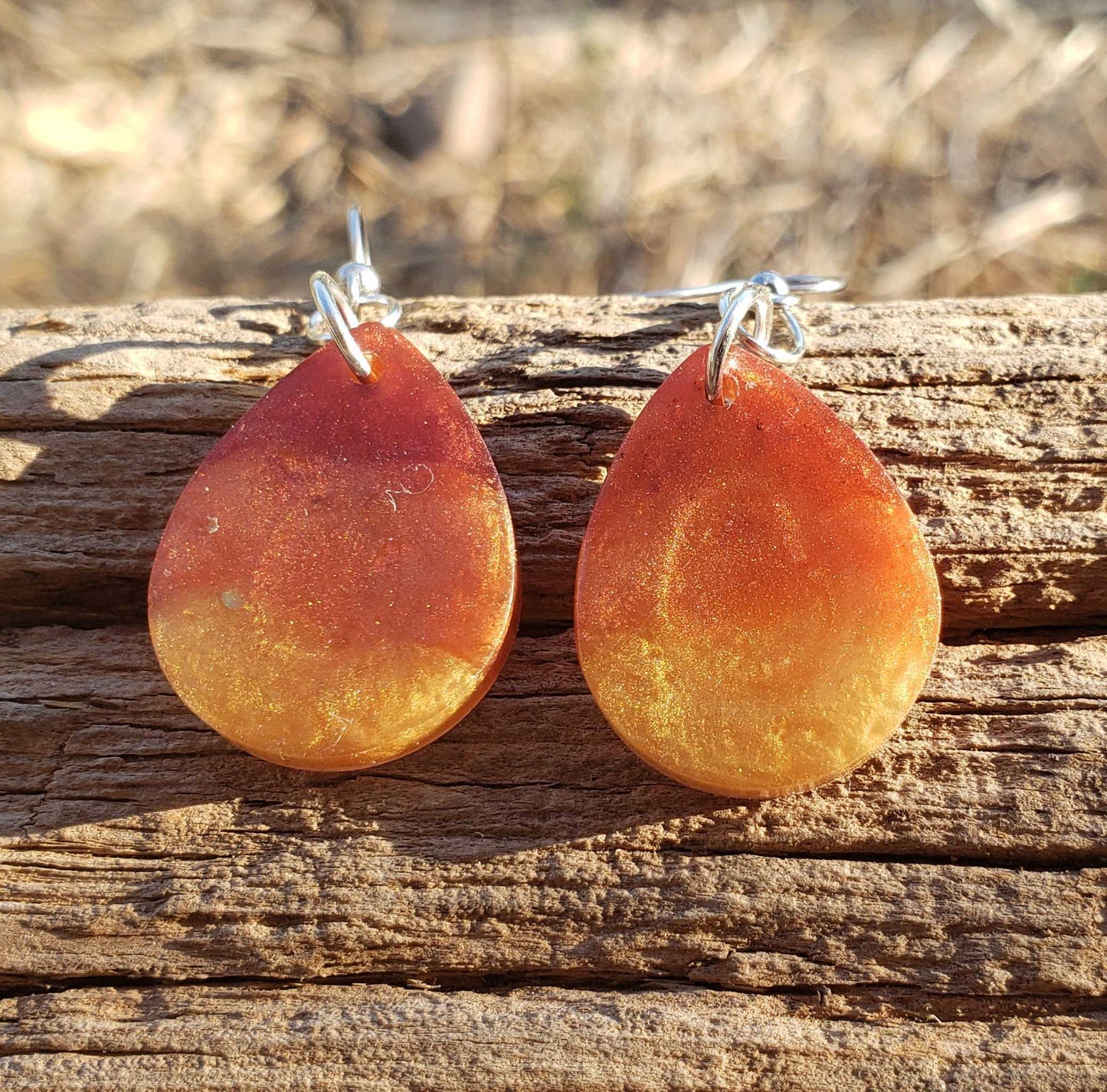 Teardrop-shaped flame fire orange earrings on a wooden surface with a blurred natural background