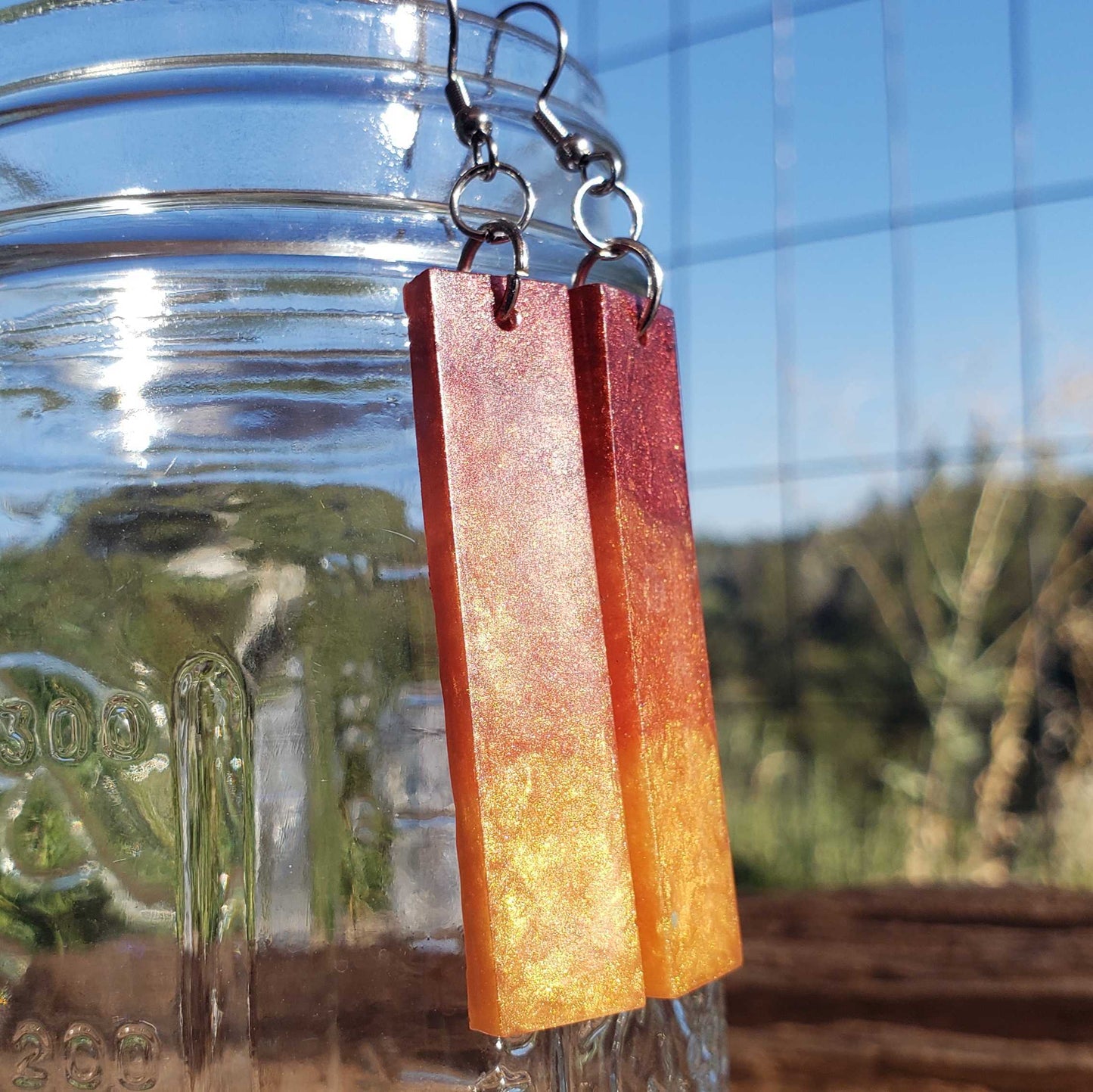 Flame colored earrings with a gradient finish hanging from a glass jar.