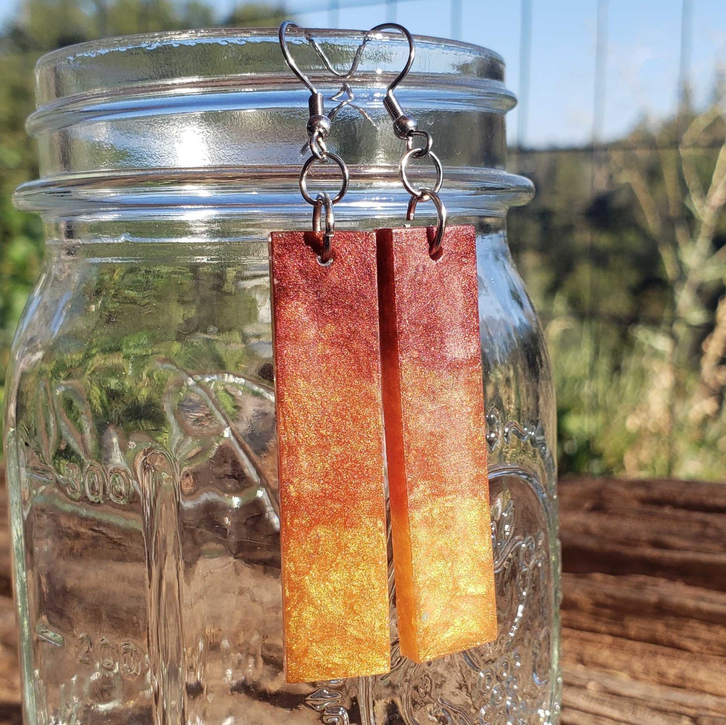 Flame fire patterned earrings hanging from a jar with a natural outdoor background
