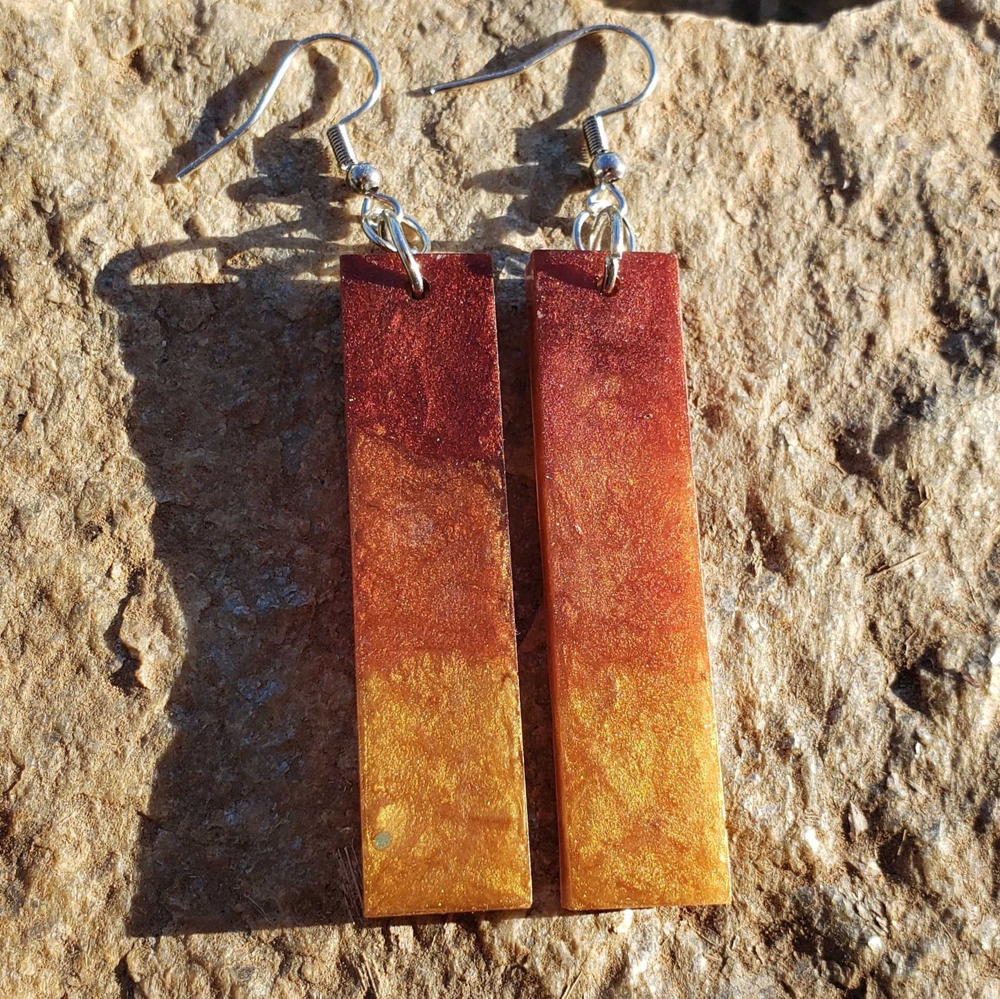 Pair of rust-colored rectangular flame earrings on a stone surface