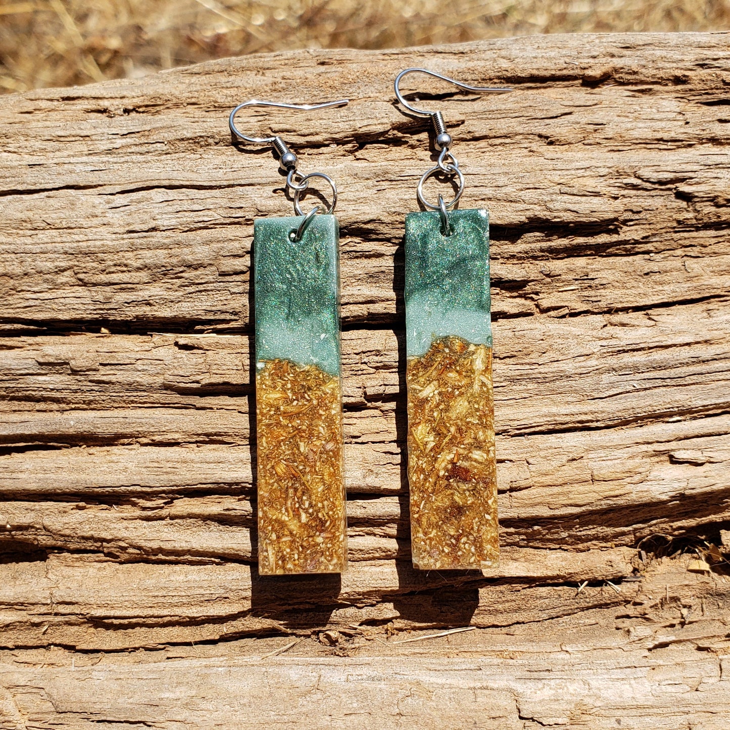 Pair of earrings with green and gold design on a wooden surface