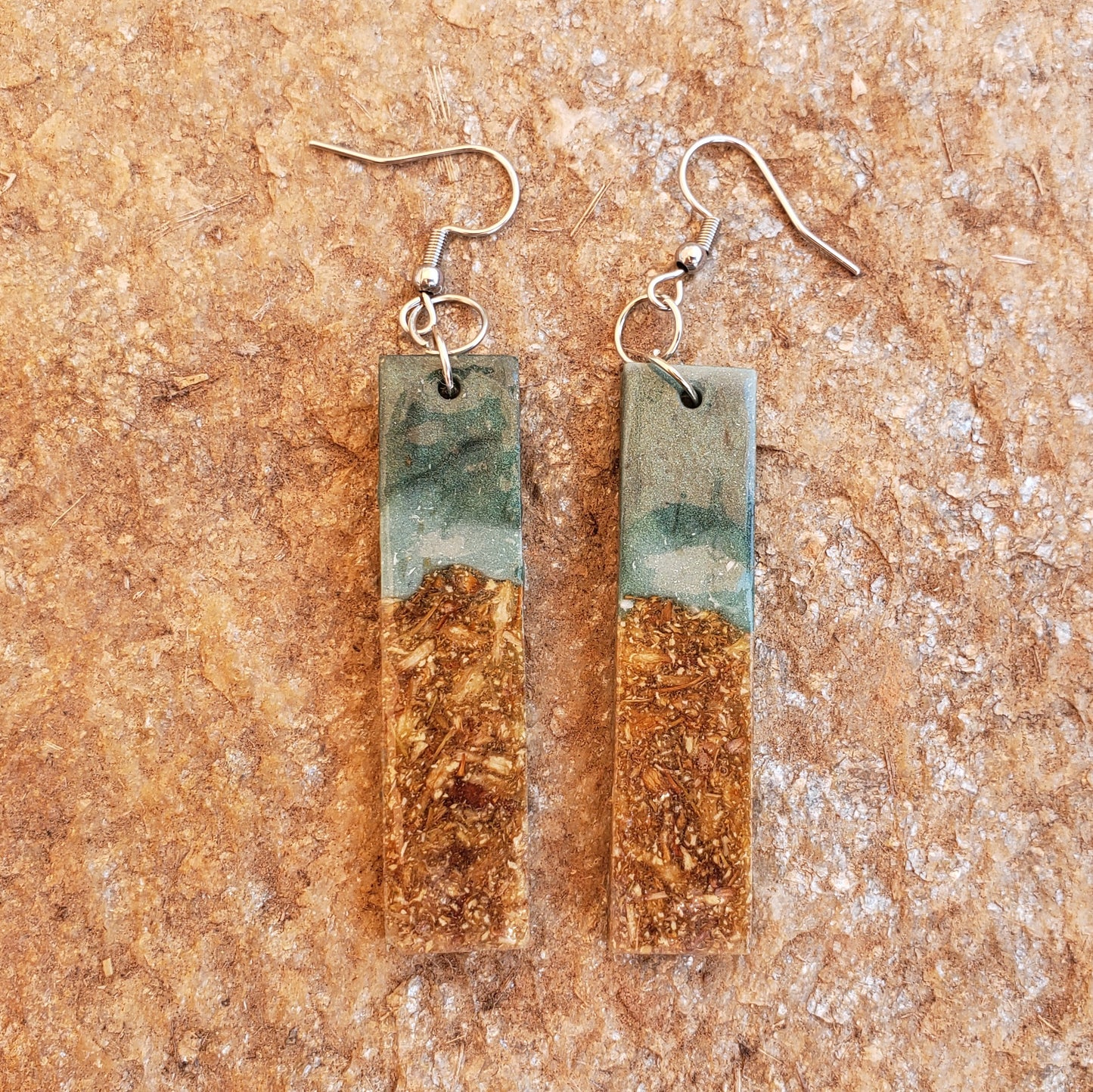 Pair of earrings with rectangular green and gold design on a textured brown surface