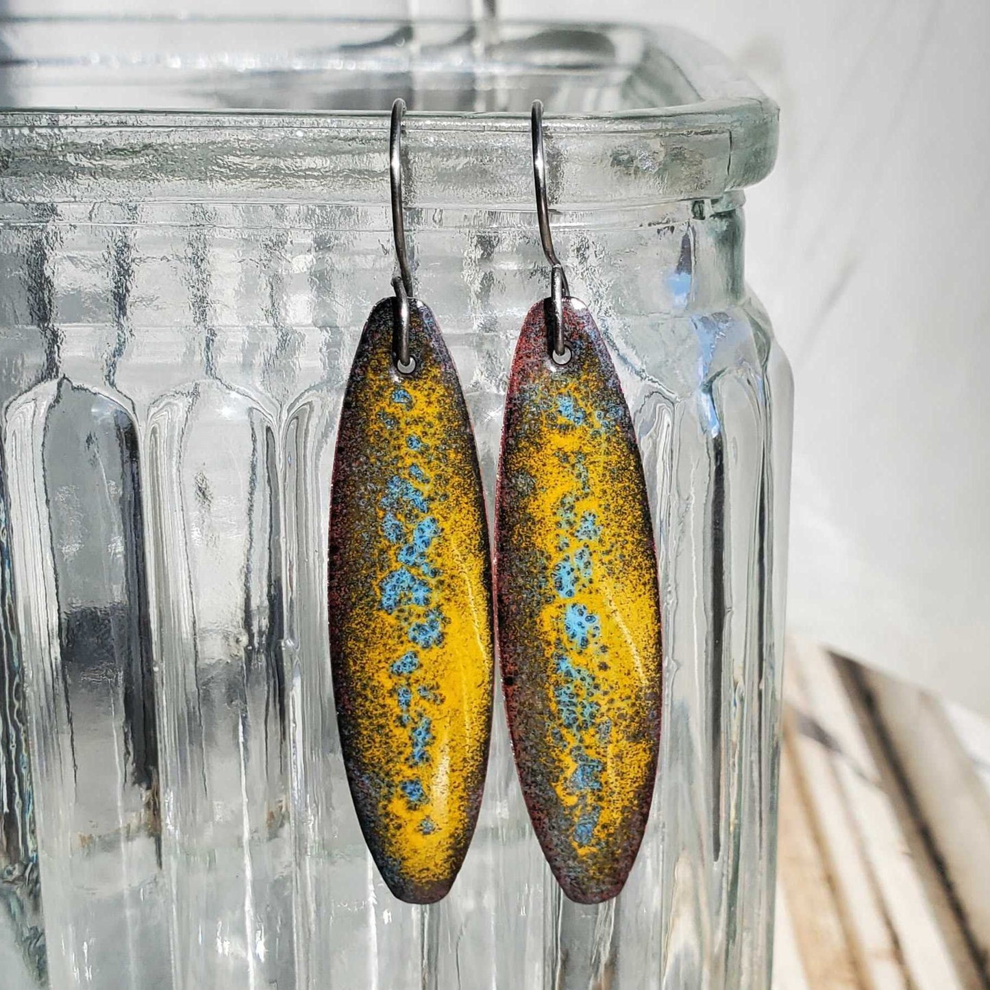 Copper earrings with a yellow and blue pattern displayed in a clear glass vase.