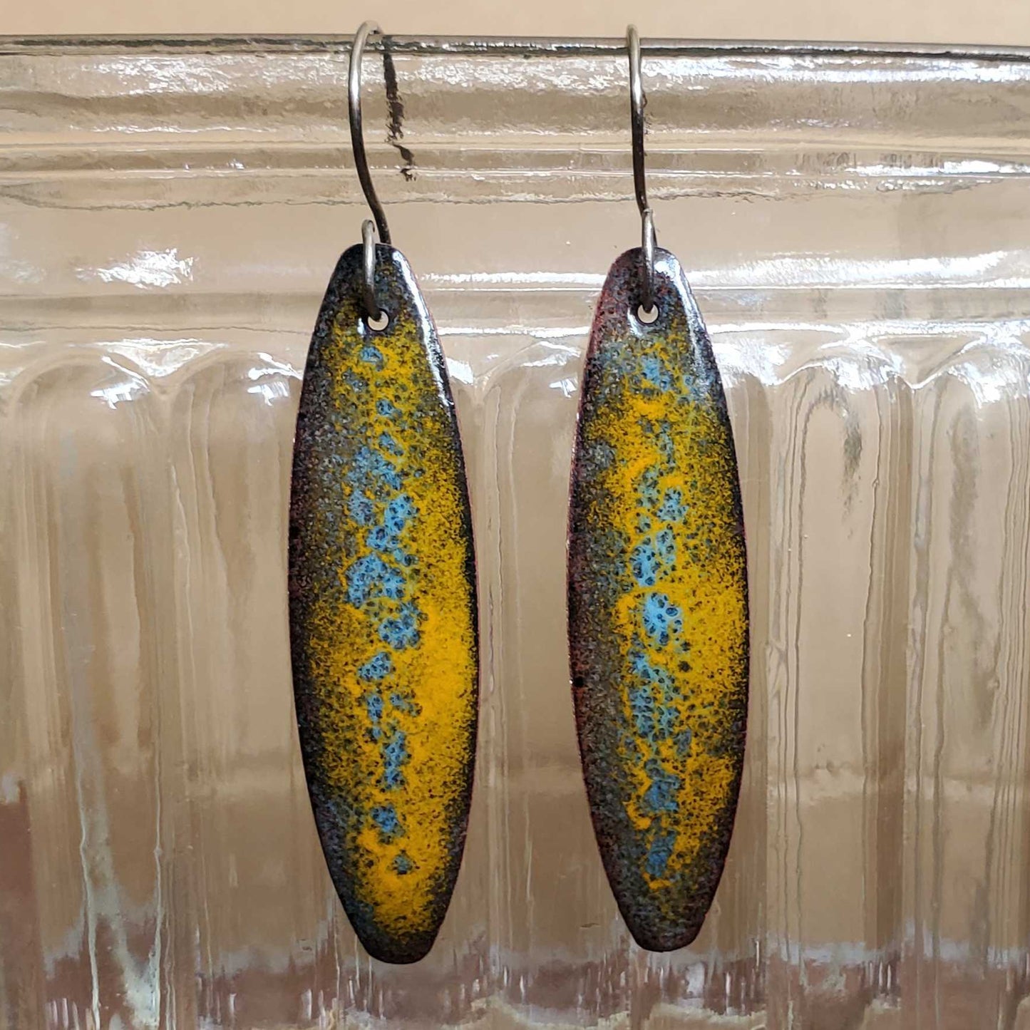 Pair of long copper earrings with a metallic-look finish hanging from a glass jar.