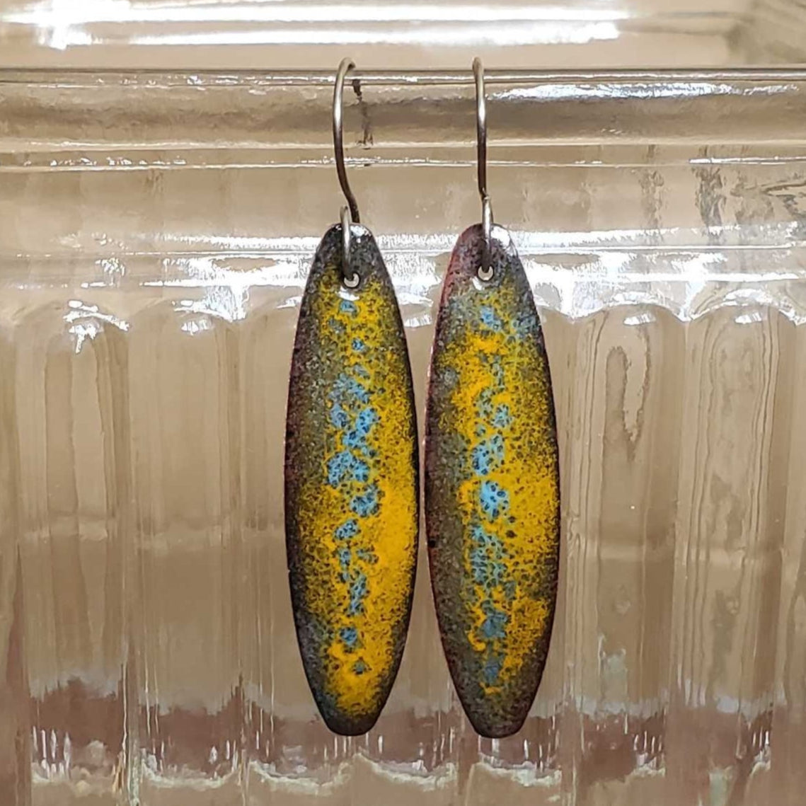 Pair of copper earrings displayed in a clear glass jar on a wooden surface.