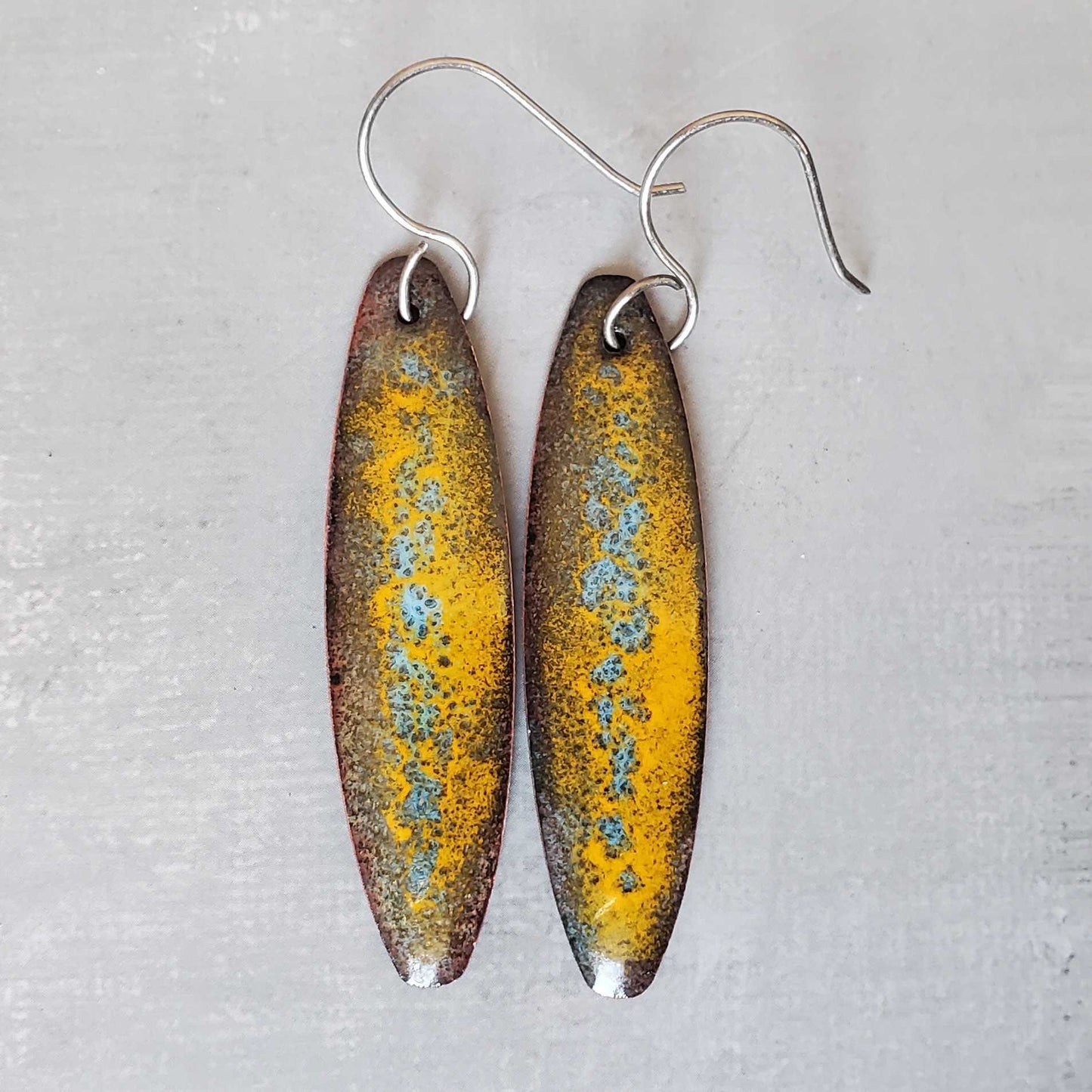 Oval-shaped copper earrings with a yellow and brown speckled design on a light gray background