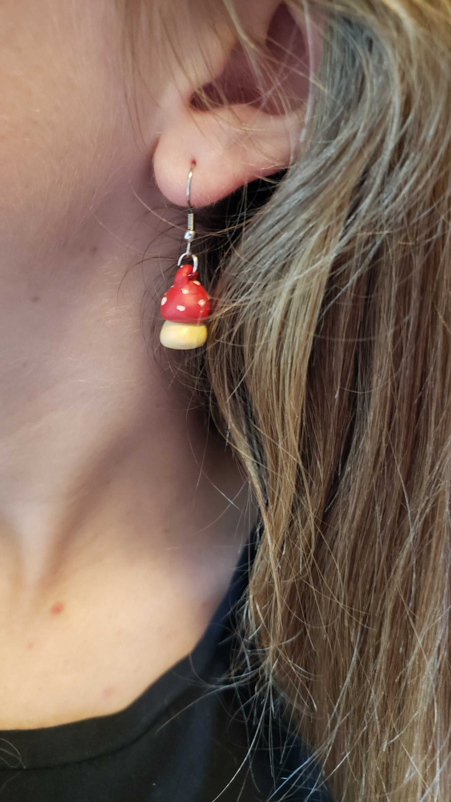 Close-up of a person wearing red and white mushroom-shaped earrings.