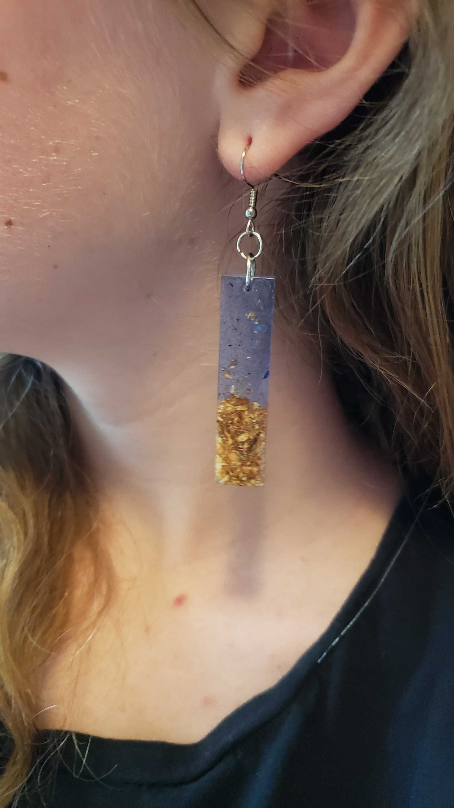 Transparent ocean-inspired dangle earring with and gold sand design made from dried flowers hanging from a person's ear.