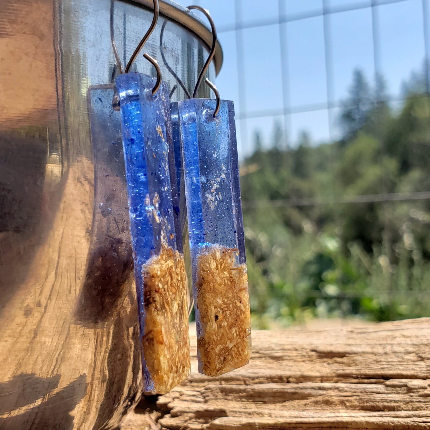 Blue and brown resin earrings hanging on a wooden surface with a blurred natural background