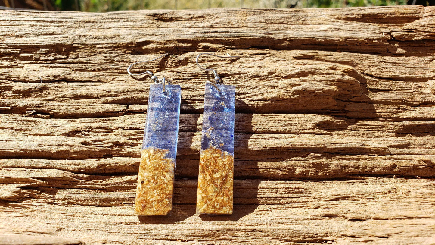 Pair of blue dangle earrings with blue and gold design on a wooden surface