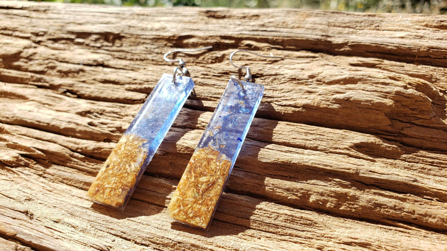 Pair of earrings with gold and blue accents on a wooden surface