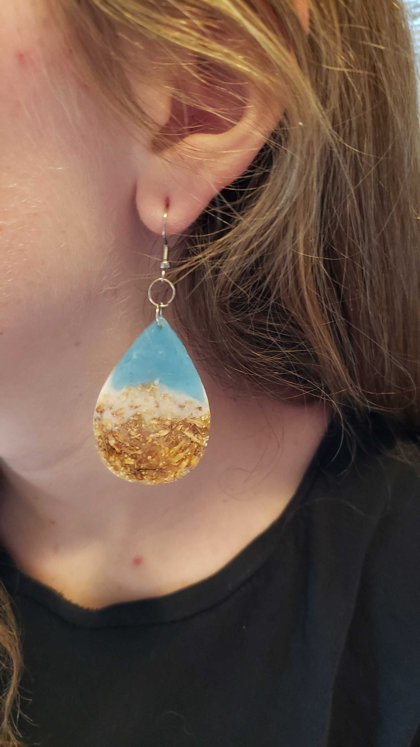 Ocean-inspired teardrop-shaped earrings worn by a person.