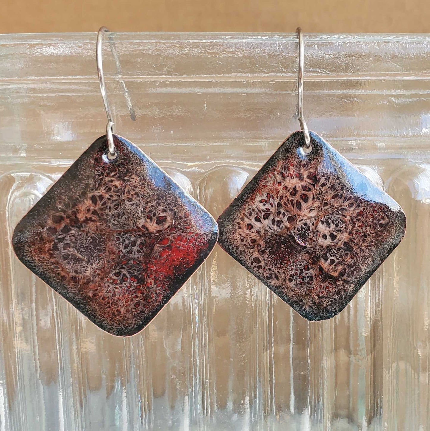 Square earrings with a textured surface on a clear glass background