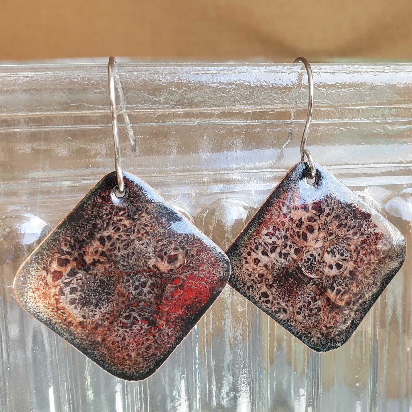 Square copper earrings with a textured surface on a clear glass background