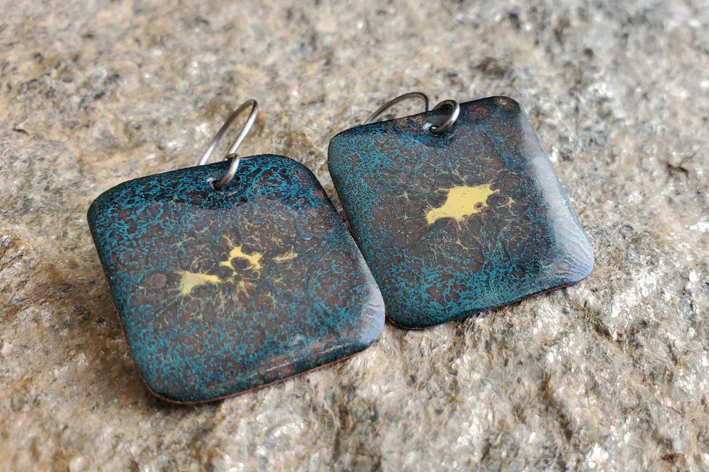 Pair of square copper enamel earrings with blue and yellow design on a textured surface