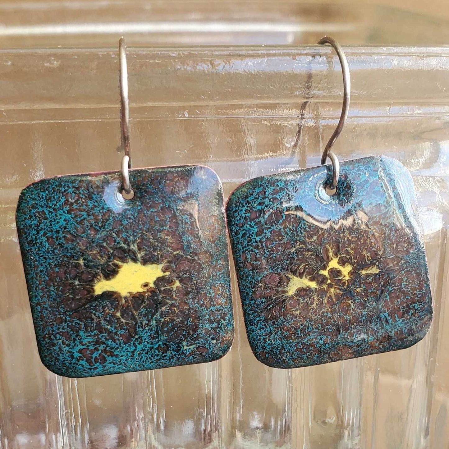 Pair of copper enamel earrings with blue and gold design on a glass surface
