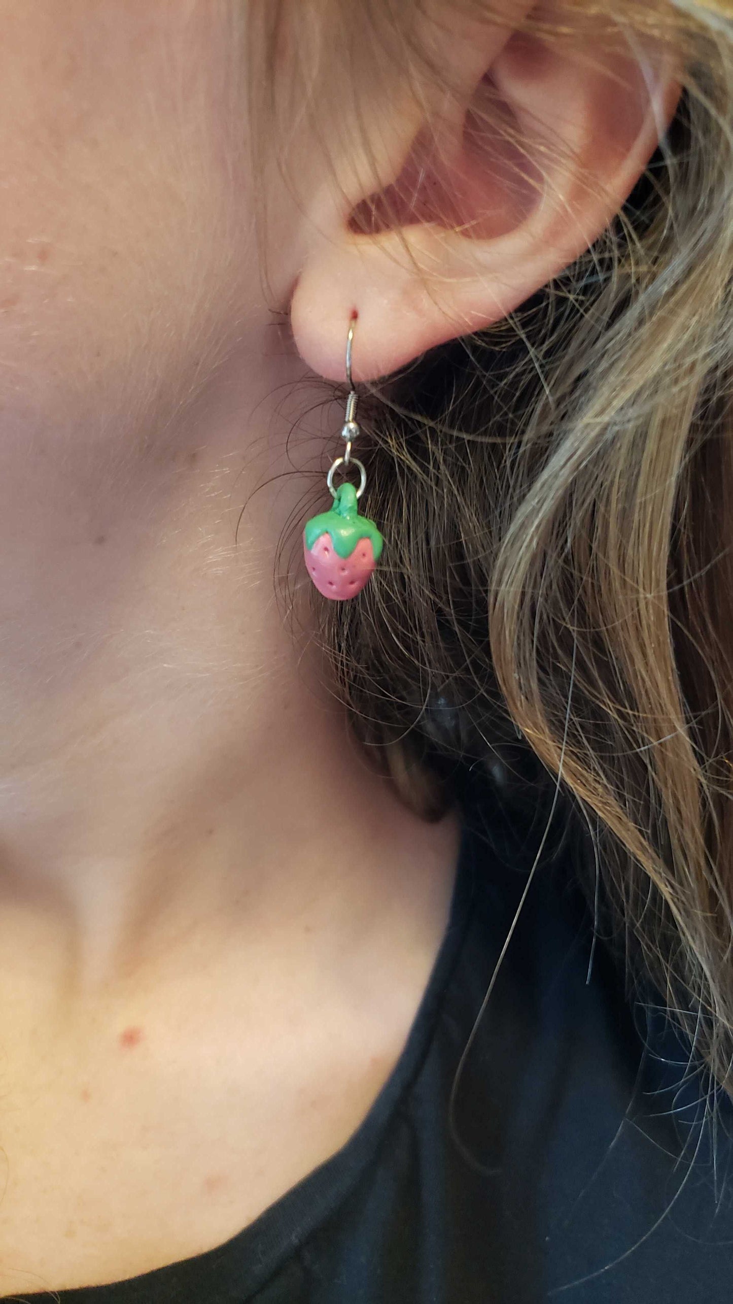 A colorful mini strawberry earring worn by a person