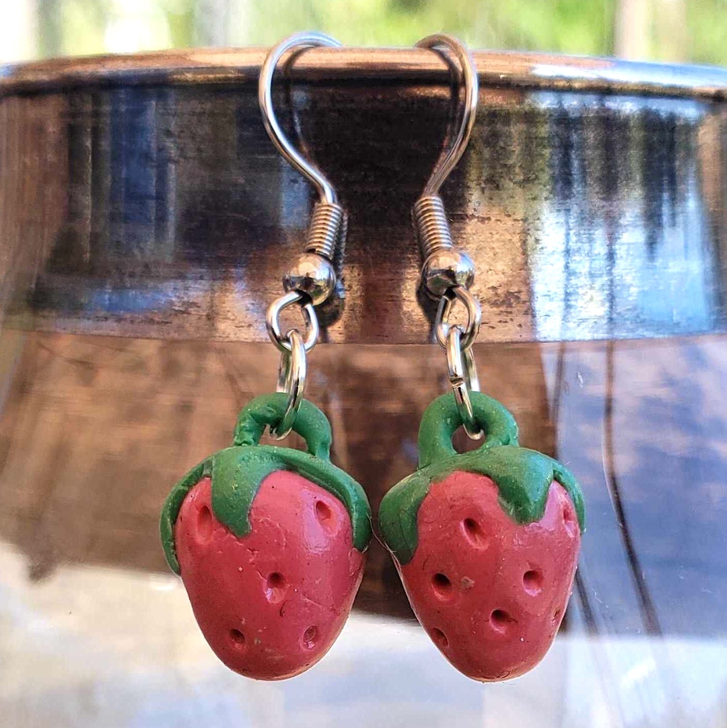 Strawberry-shaped earrings with green tops on a metallic surface