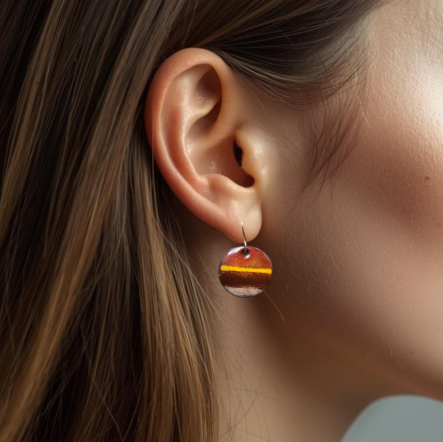Close-up of an ear wearing a round earring with a brown and yellow sstriped design.