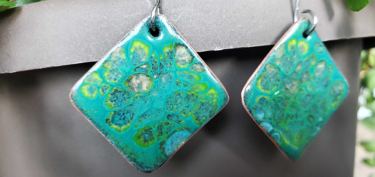 Pair of square-shaped copper earrings with green and blue pattern on a gray background