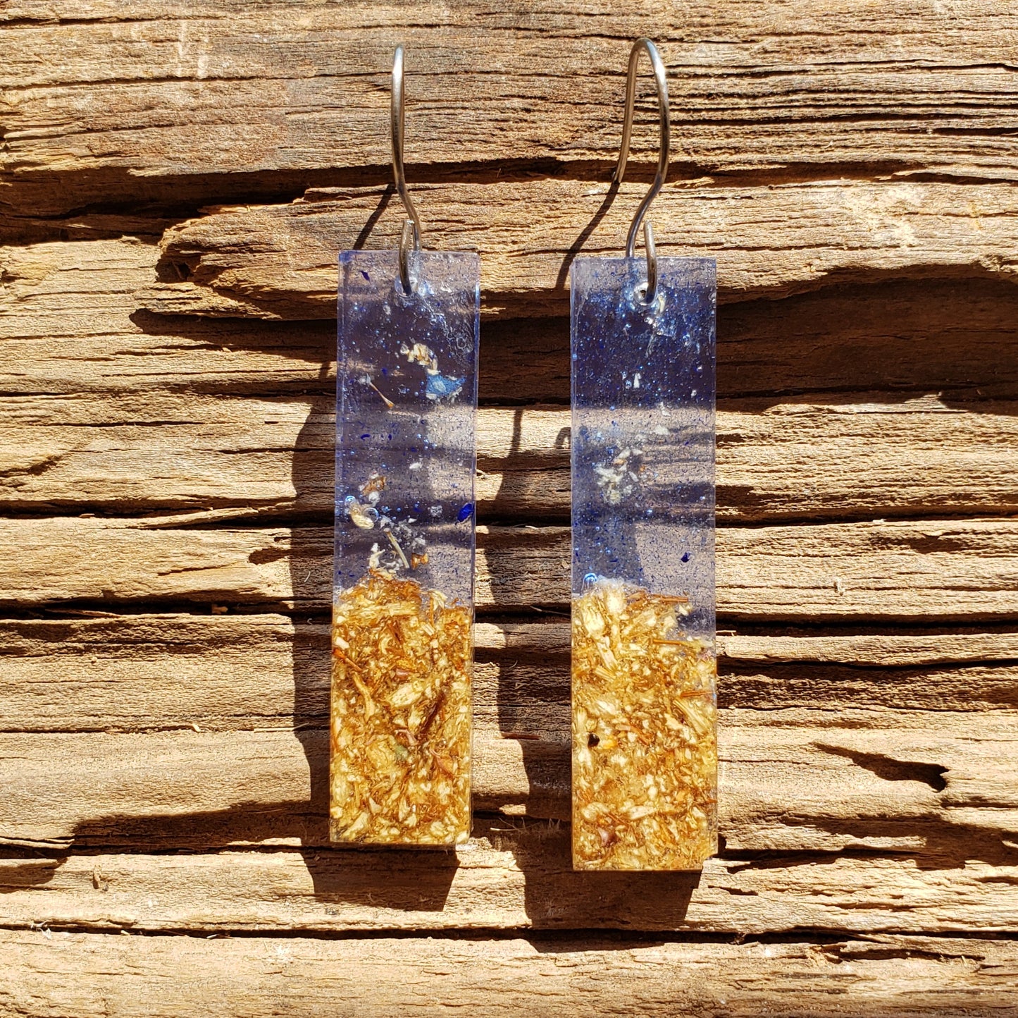 Pair of dried florwer earrings with blue and gold design on a wooden surface