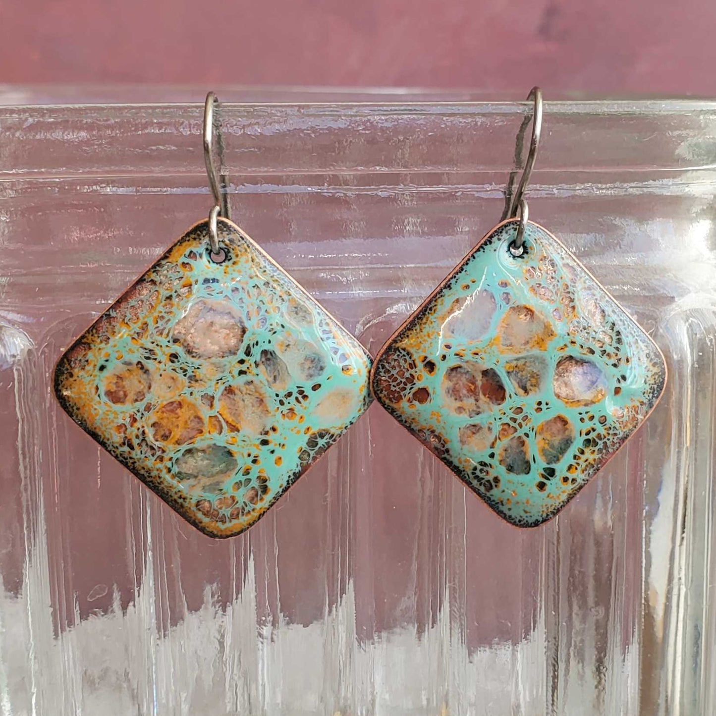 Square-shaped earrings with a decorative pattern on a glass jar.