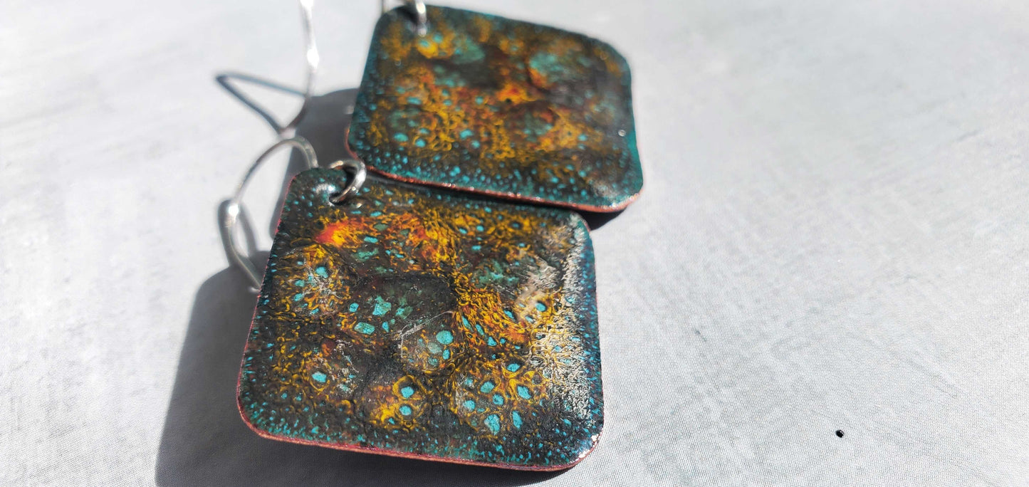 Pair of square copper earrings with a textured, multicolored surface on a light background