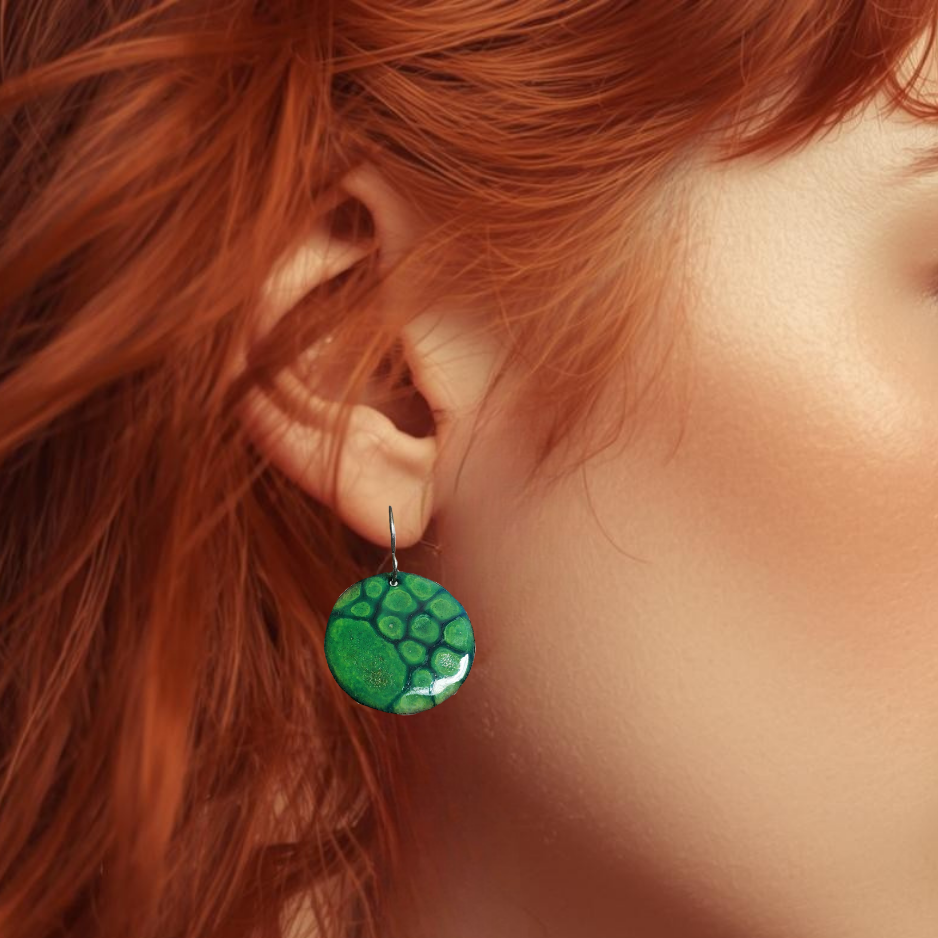 Close-up of a person wearing green patterned copper enamel earrings with red hair.