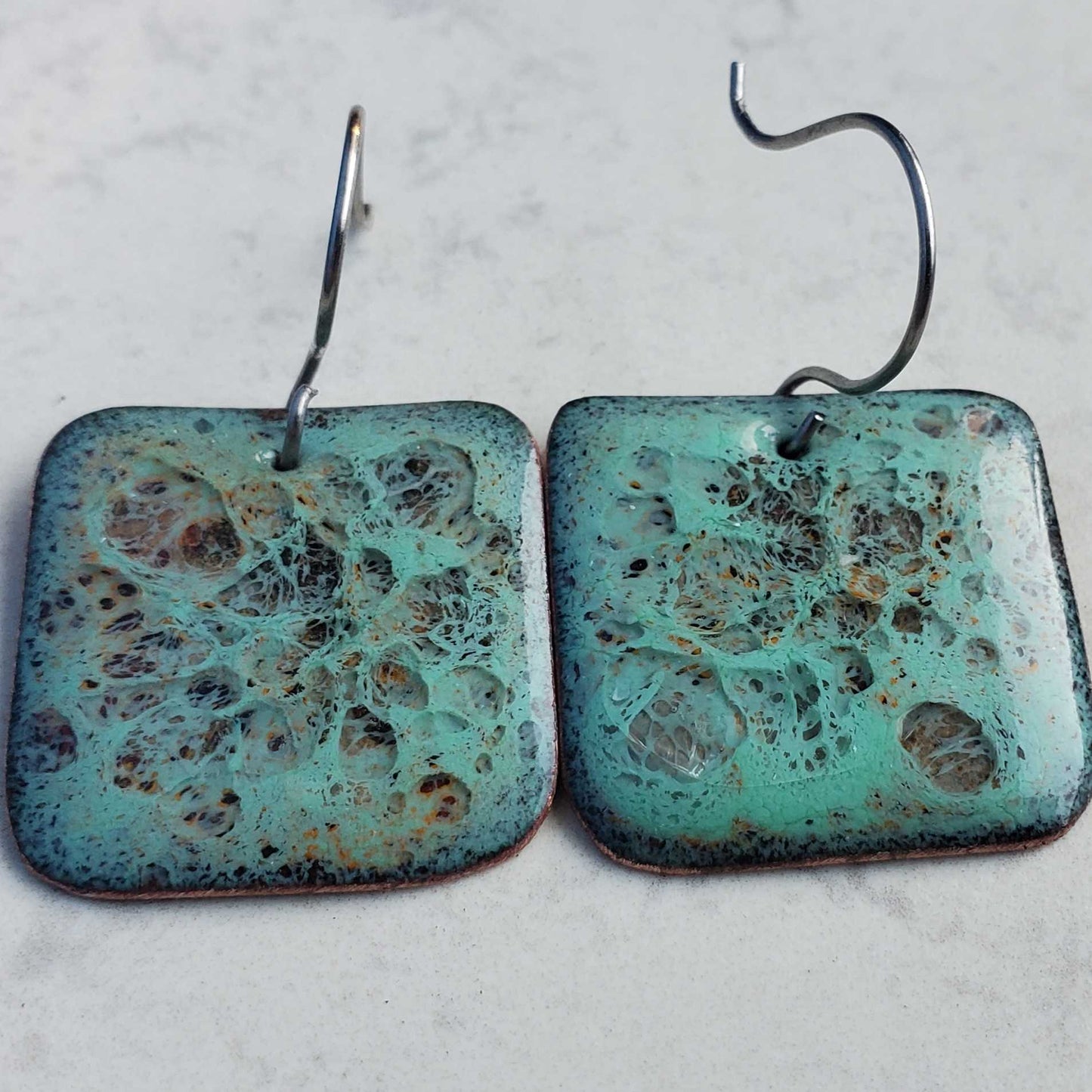 Pair of square copper earrings with textured turquoise surface on a light gray background