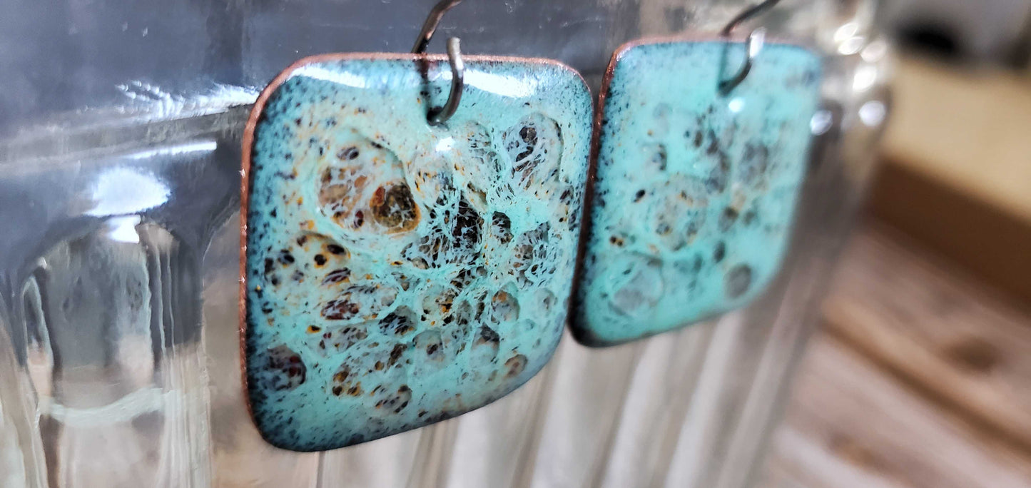 Turquoise copper and glass earrings with speckled design on a blurred background