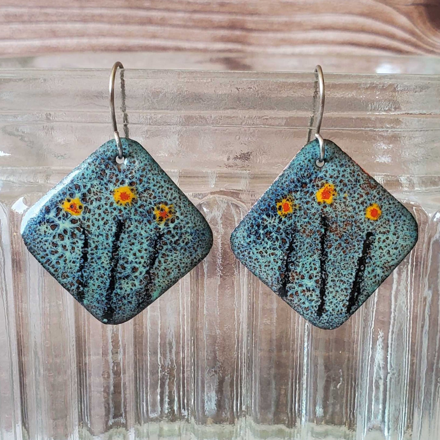 Square copper earrings with floral design on a wooden surface