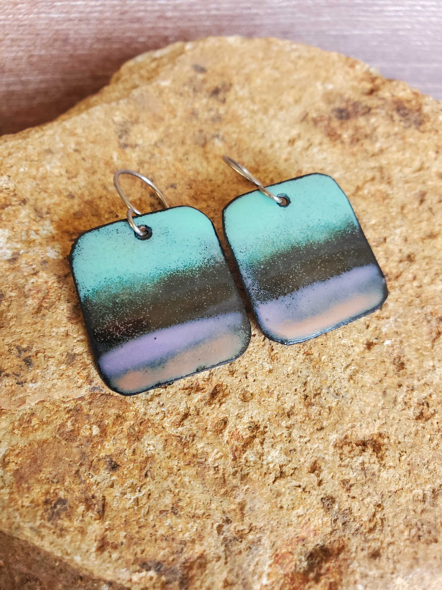 Square copper enamel earrings with gradient color on a stone surface