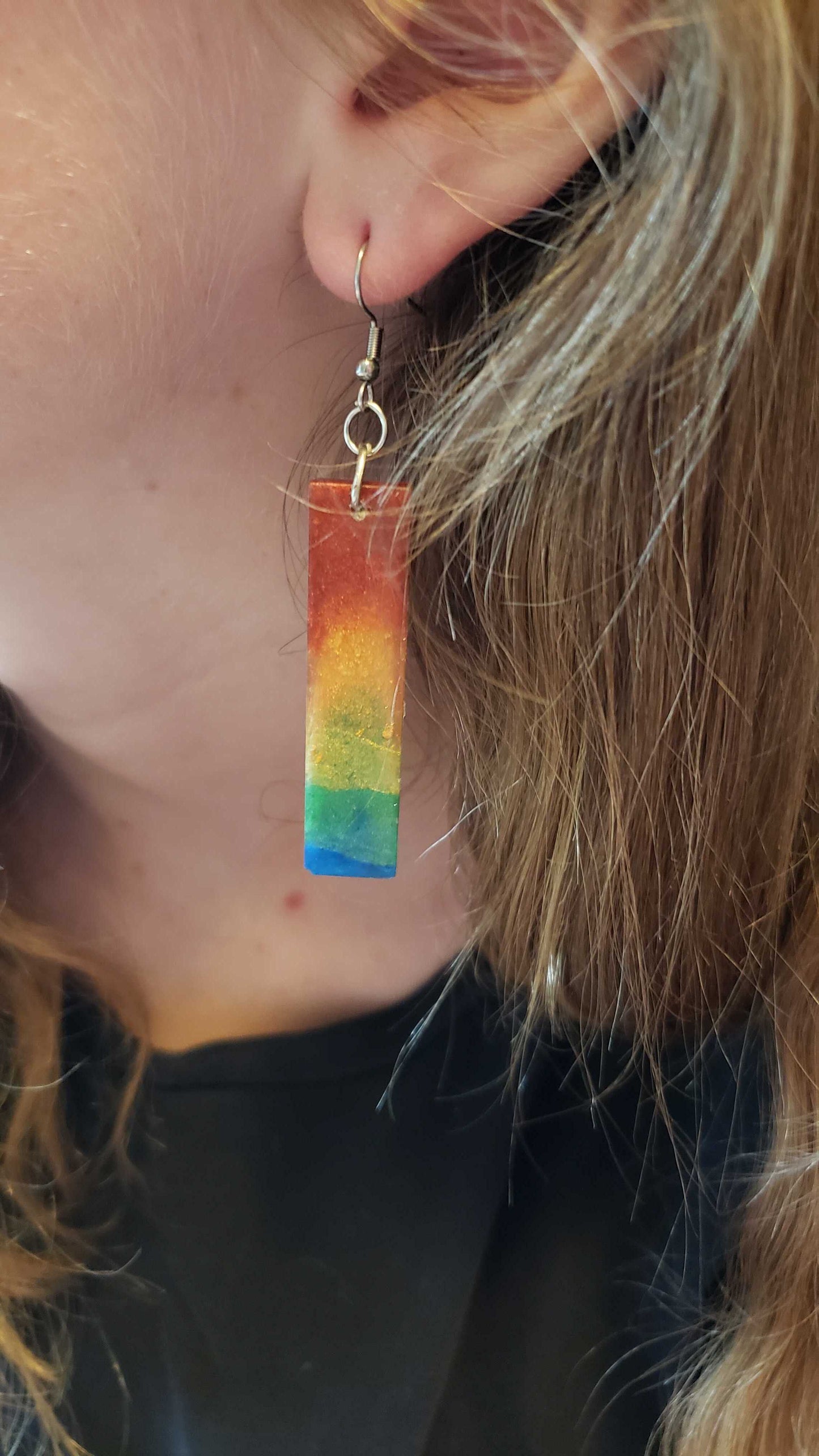 Close-up of a rainbow-colored earring worn by a person with blonde hair.