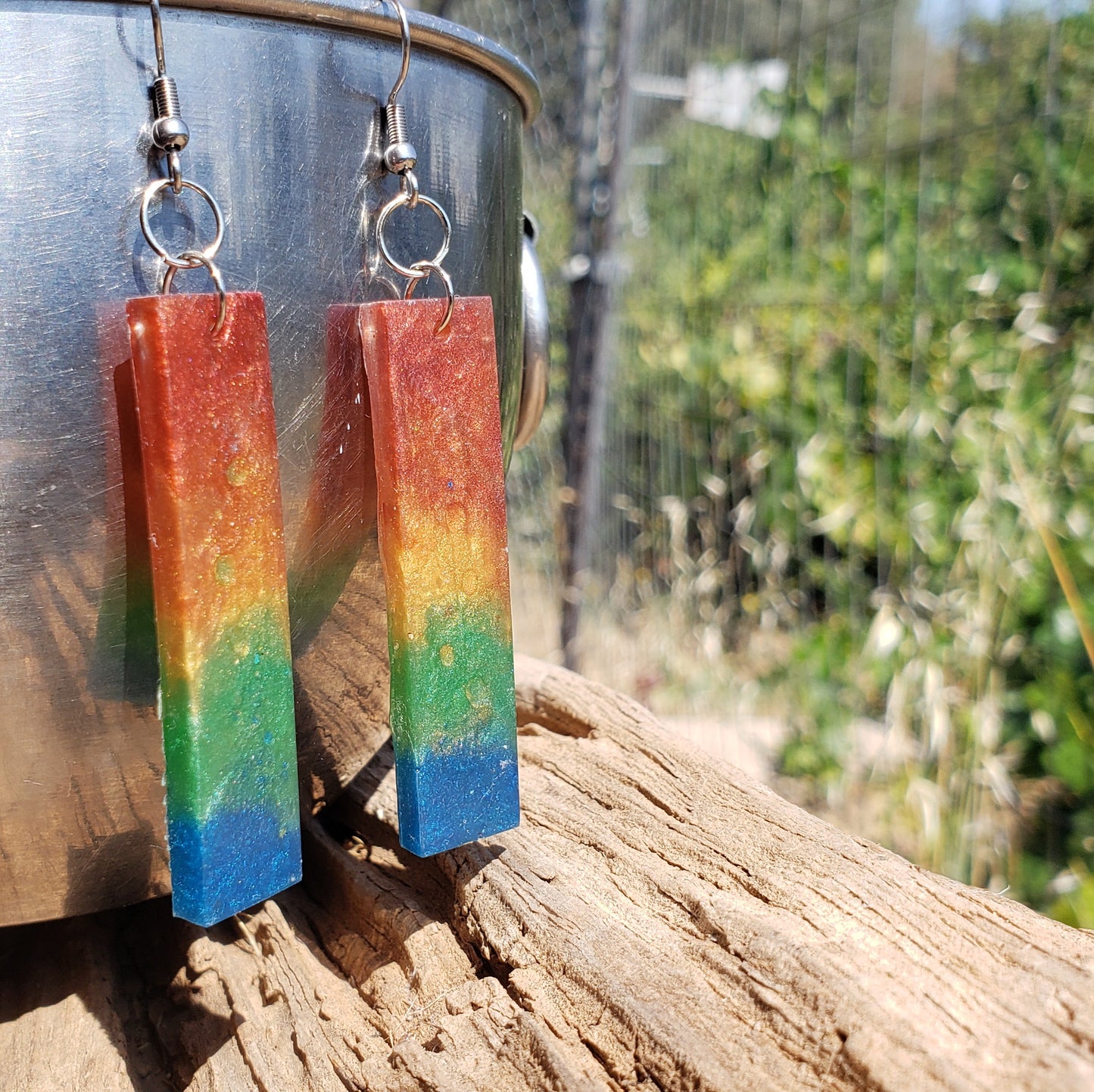 Rainbow earrings hanging on a metal surface with a natural background
