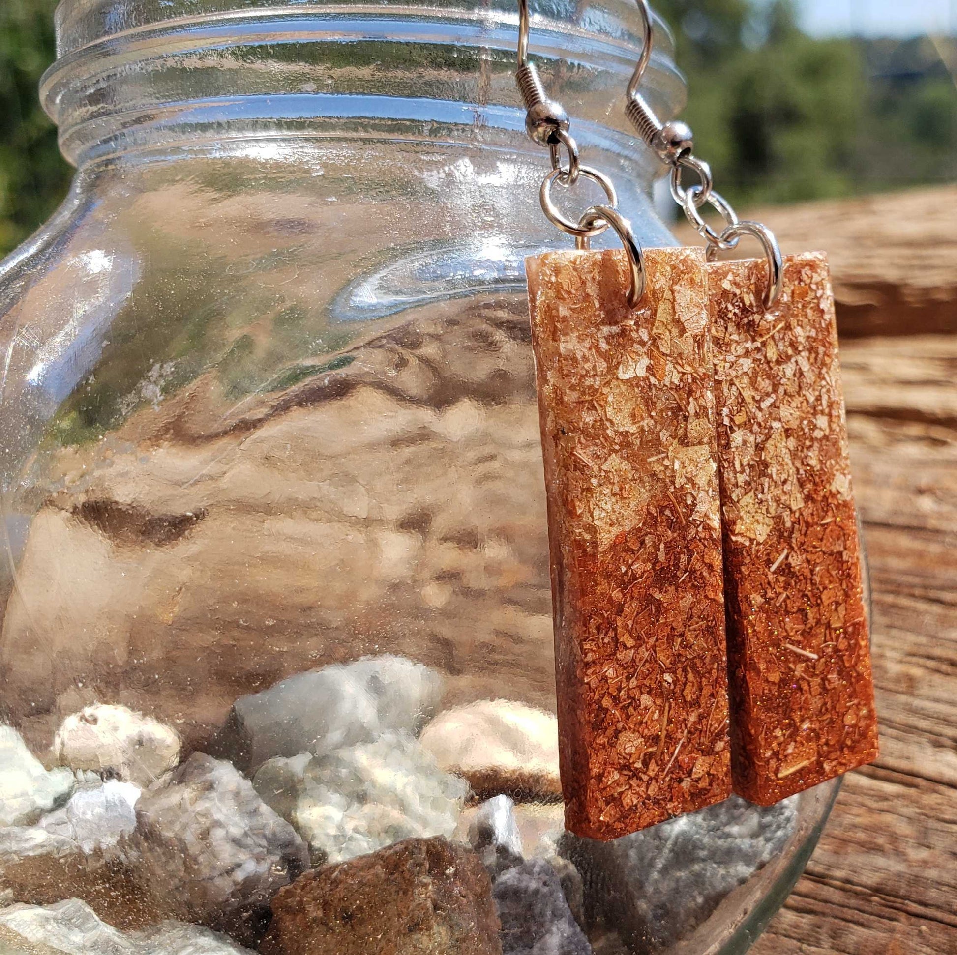 Dried leaf earrings hanging from a glass jar with a natural background