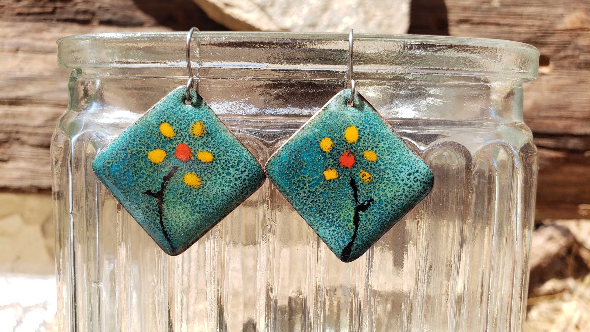 Pair of square copper earrings with floral design on a glass jar.