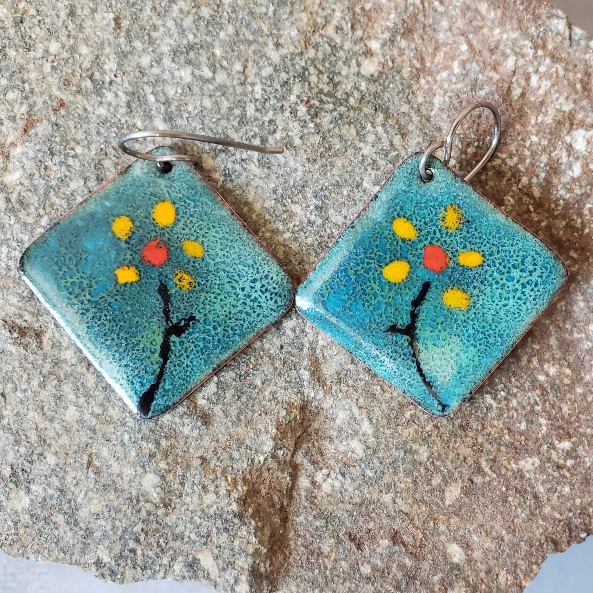 Pair of turquoise copper enamel square earrings with floral design on a stone surface