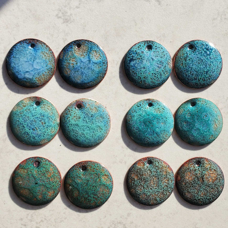 Six pairs of blue copper earrings with a speckled cosmic pattern on a light gray surface.
