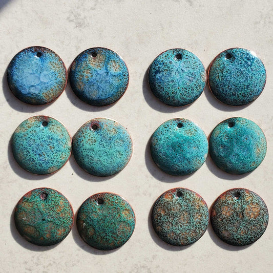 Six pairs of blue copper earrings with a speckled cosmic pattern on a light gray surface.