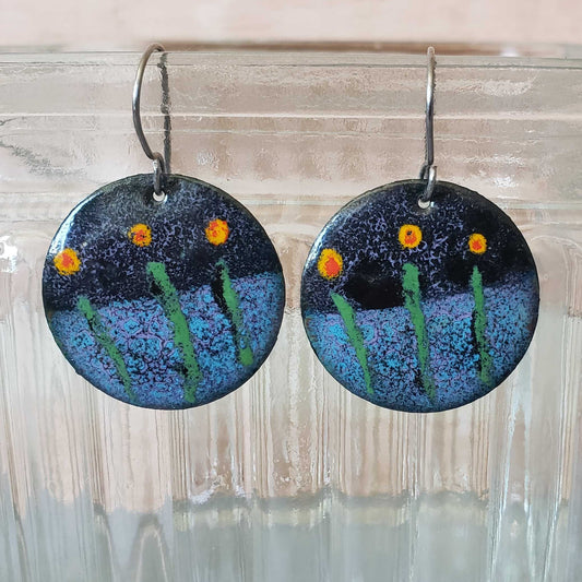 Round copper earrings with floral design hanging from a glass jar.