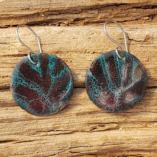 Pair of round copper enamel earrings with a textured design on a wooden surface