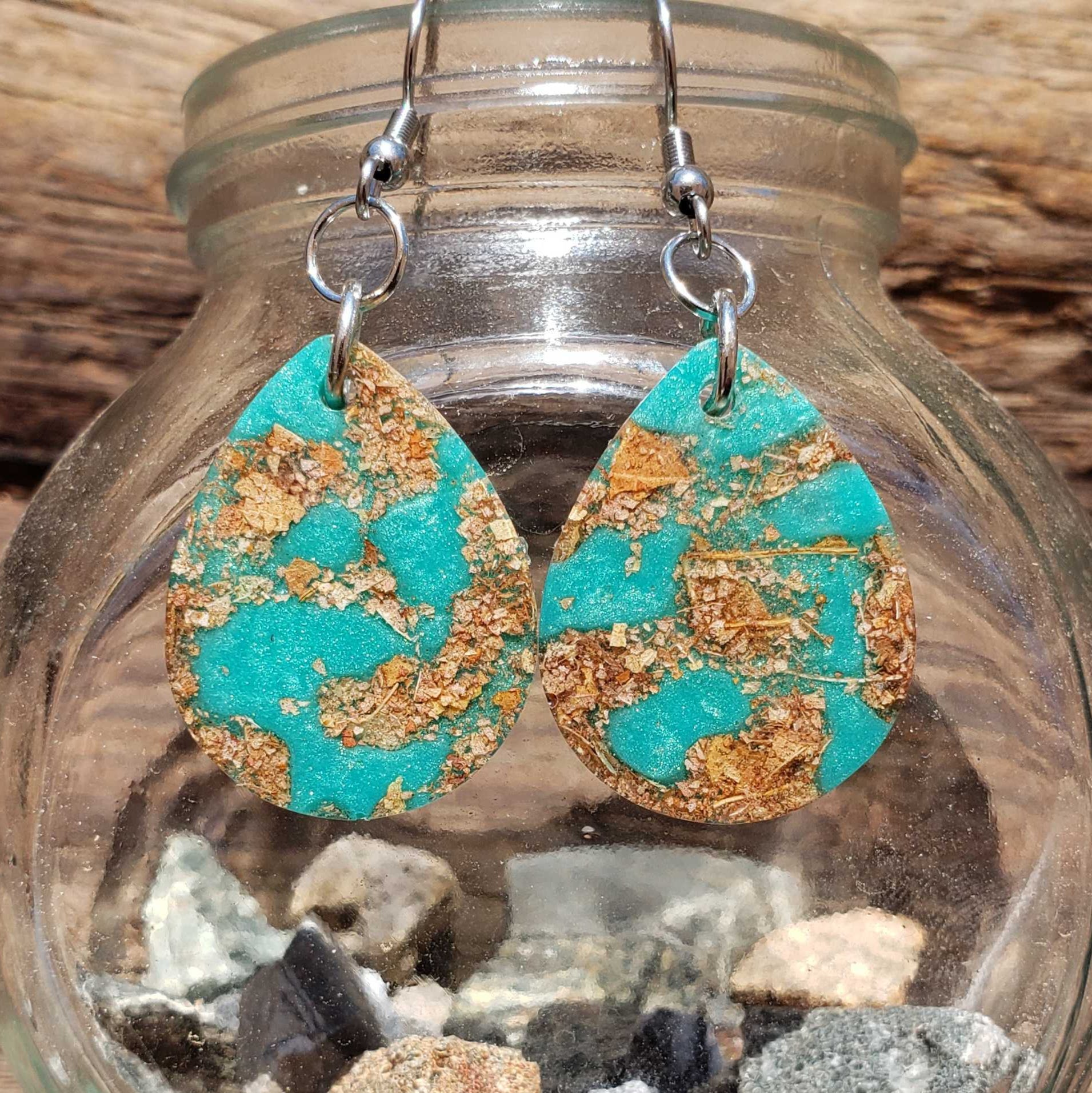 Boho turquoise and gold teardrop earrings made from dried leaves on a glass jar with stones