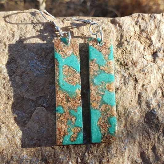 Turquoise and brown patterned earrings made from dried leaves on a stone surface
